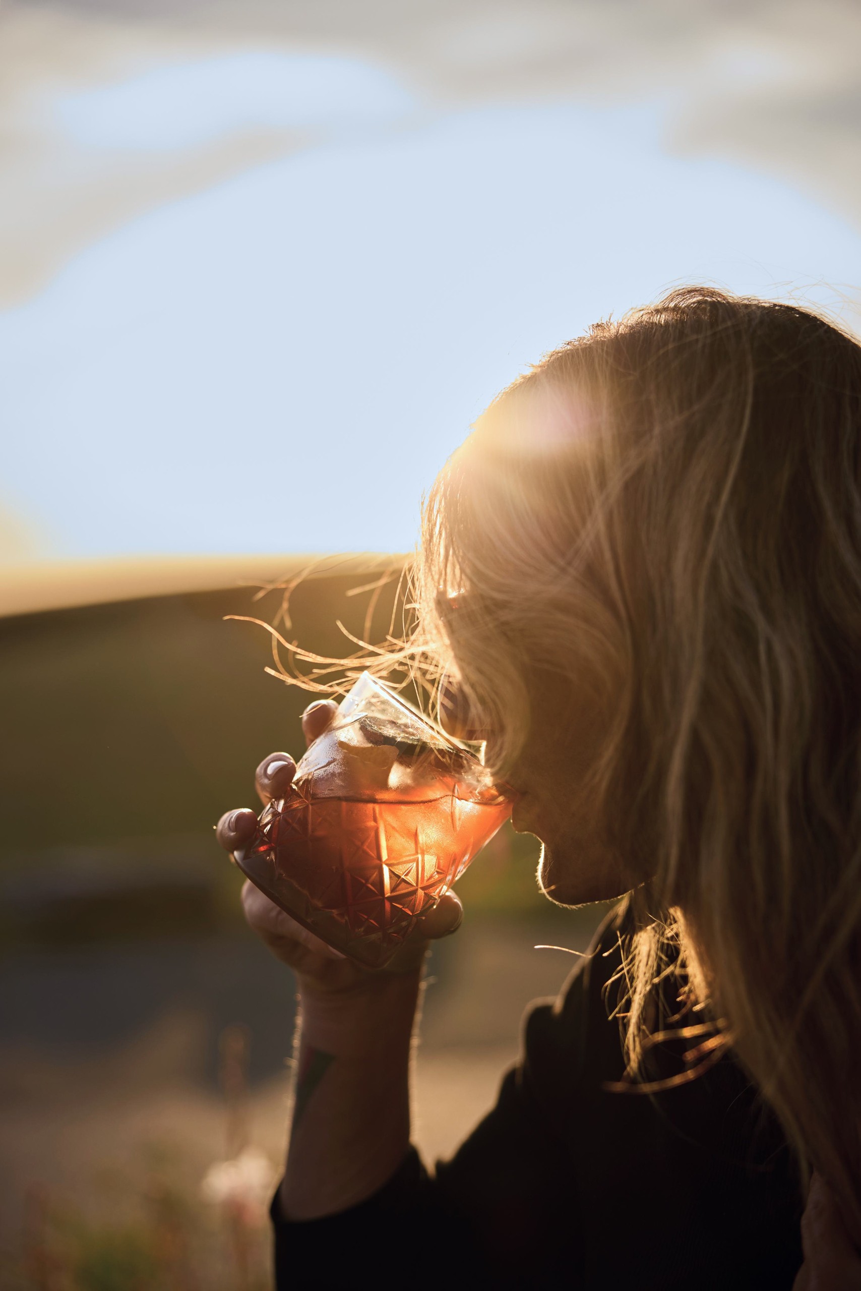 Woman sipping from a cut-glass tumbler in the low winter sun