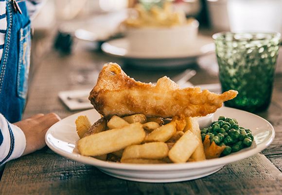 An image of fish, chips and peas on a white plate. 